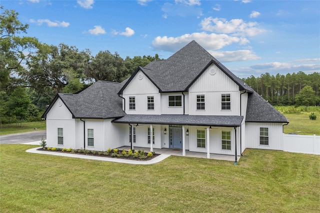 modern inspired farmhouse featuring a shingled roof, a front yard, covered porch, and fence