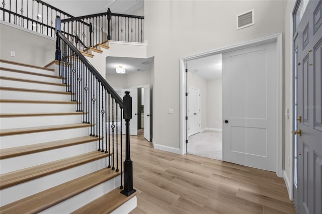 foyer entrance featuring visible vents, stairway, a high ceiling, light wood-type flooring, and baseboards