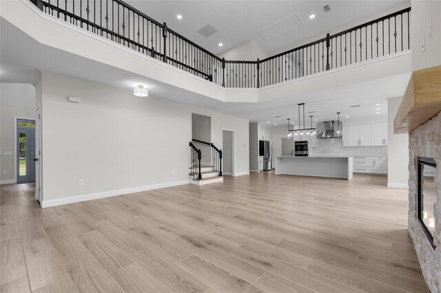 unfurnished living room featuring a stone fireplace, light wood finished floors, a towering ceiling, and baseboards