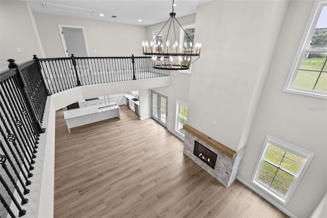 living room featuring a towering ceiling, attic access, a glass covered fireplace, wood finished floors, and a chandelier