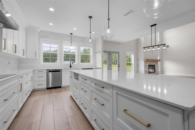 kitchen with stainless steel dishwasher, wood tiled floor, white cabinets, a stone fireplace, and wall chimney range hood