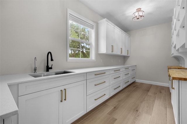 kitchen featuring baseboards, wood counters, light wood-type flooring, white cabinetry, and a sink