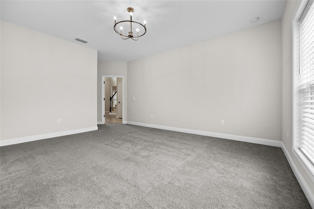 carpeted spare room with baseboards, visible vents, and a notable chandelier