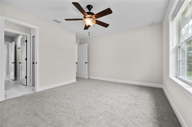 carpeted empty room with a wealth of natural light, a ceiling fan, visible vents, and baseboards