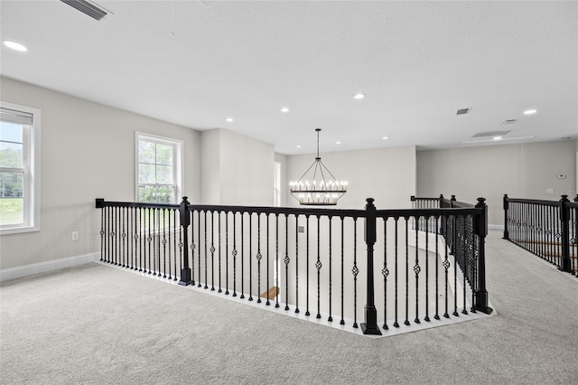 hallway featuring a notable chandelier, visible vents, baseboards, and carpet flooring