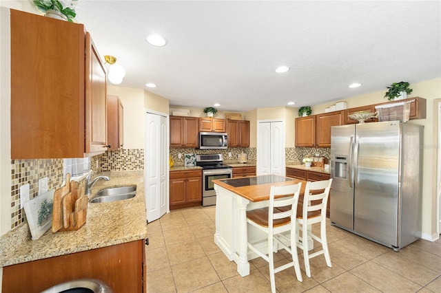 kitchen with brown cabinets, light tile patterned floors, stainless steel appliances, a sink, and light stone countertops