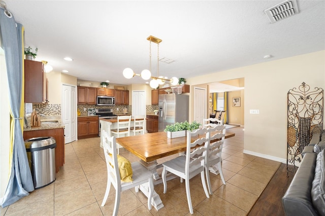 dining space with baseboards, light tile patterned flooring, visible vents, and an inviting chandelier