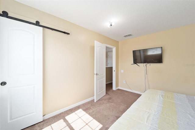 unfurnished bedroom featuring carpet, visible vents, baseboards, and a barn door