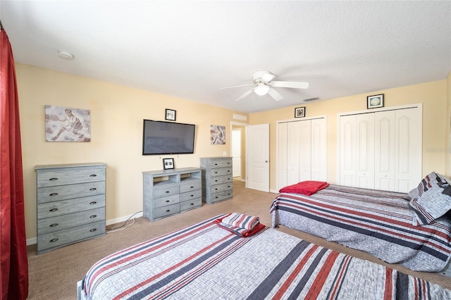 carpeted bedroom with two closets, visible vents, ceiling fan, a textured ceiling, and baseboards