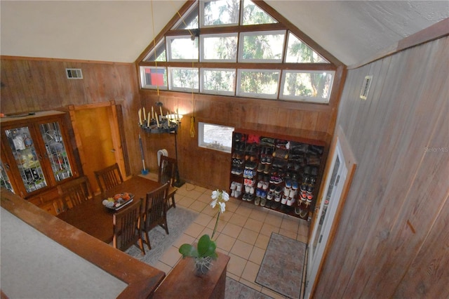 tiled dining space featuring lofted ceiling, wood walls, a healthy amount of sunlight, and visible vents