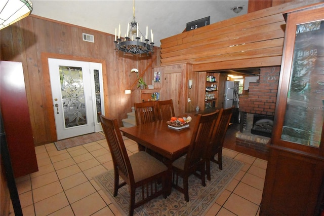 tiled dining space featuring visible vents, wood walls, and an inviting chandelier