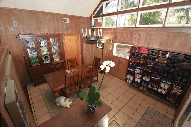 tiled dining space with vaulted ceiling, a healthy amount of sunlight, wood walls, and visible vents