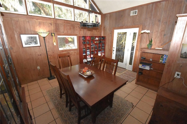 dining room featuring wood walls, tile patterned flooring, visible vents, and vaulted ceiling