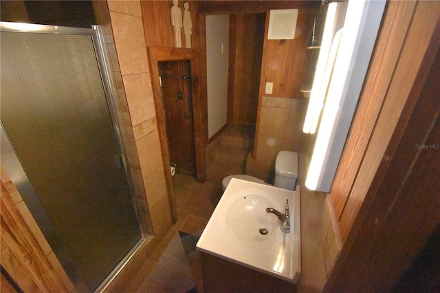 bathroom featuring a stall shower, toilet, vanity, wood walls, and tile walls