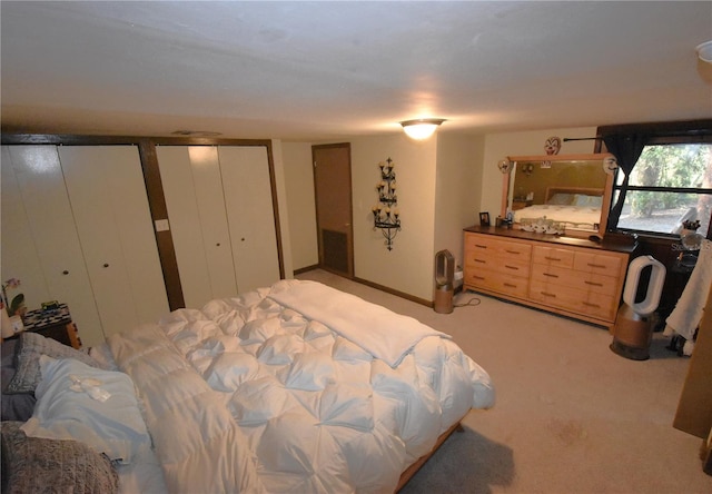 bedroom with light colored carpet, baseboards, and two closets