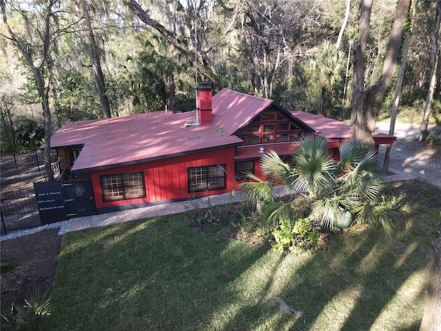 view of front facade with a chimney, a front yard, fence, and a view of trees