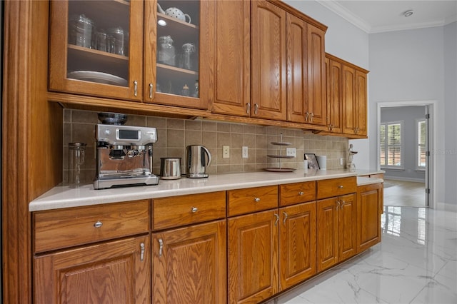 kitchen featuring marble finish floor, ornamental molding, tasteful backsplash, brown cabinetry, and glass insert cabinets