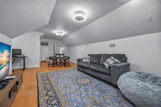 living room featuring vaulted ceiling, light wood-type flooring, visible vents, and baseboards