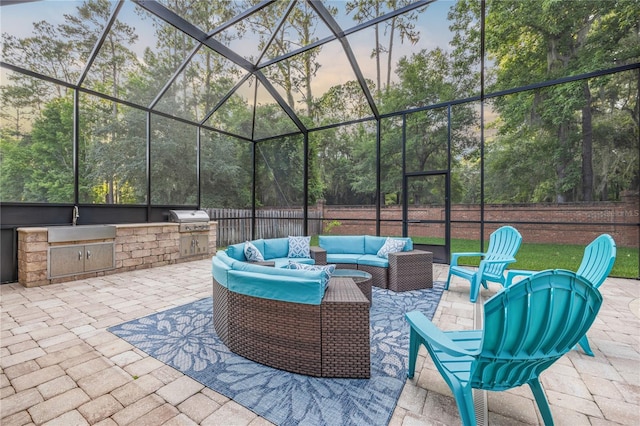 patio terrace at dusk with a lanai, outdoor lounge area, a grill, and a sink