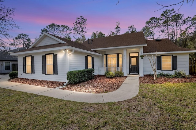 single story home with a porch, roof with shingles, and a front yard