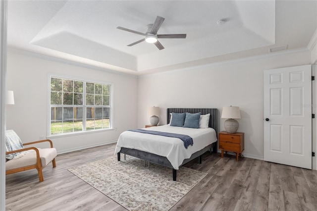 bedroom with ornamental molding, a raised ceiling, baseboards, and wood finished floors