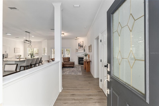 foyer entrance featuring light wood finished floors, a glass covered fireplace, visible vents, and crown molding