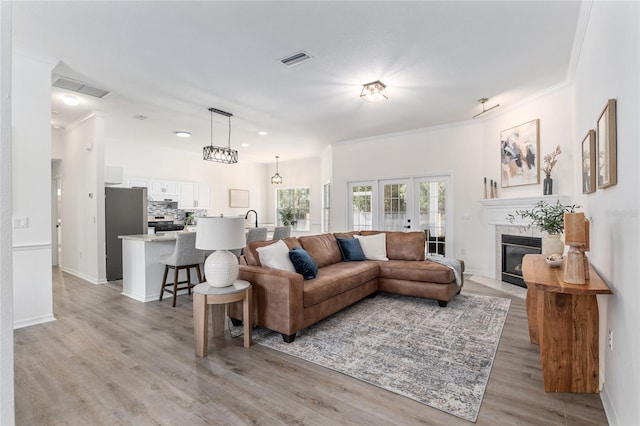 living area with light wood-style floors, a fireplace with flush hearth, visible vents, and french doors