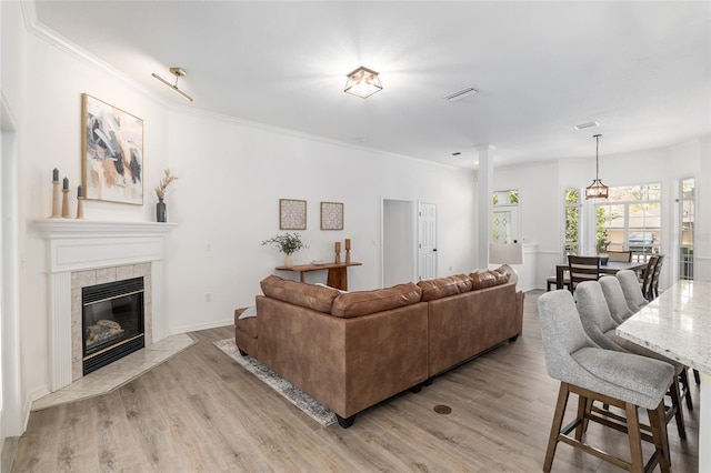 living area with light wood-type flooring, visible vents, crown molding, and a tile fireplace