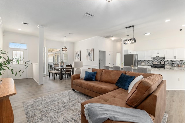 living area featuring baseboards, decorative columns, visible vents, and light wood-style floors