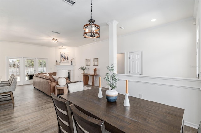 dining space with visible vents, light wood-style floors, a glass covered fireplace, ornamental molding, and ornate columns