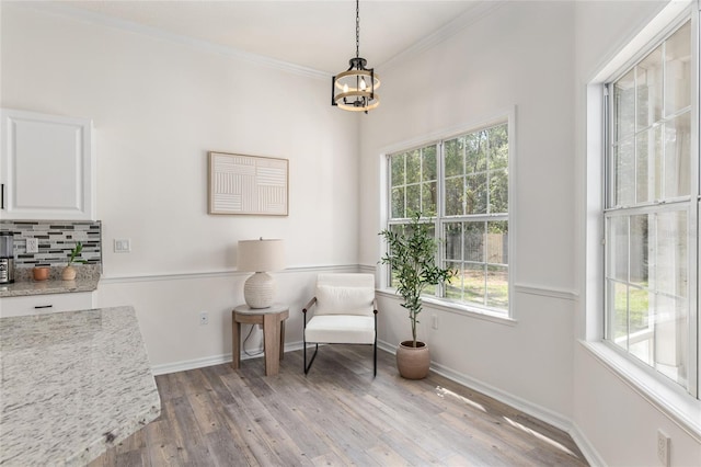 living area featuring an inviting chandelier, light wood-style flooring, ornamental molding, and baseboards