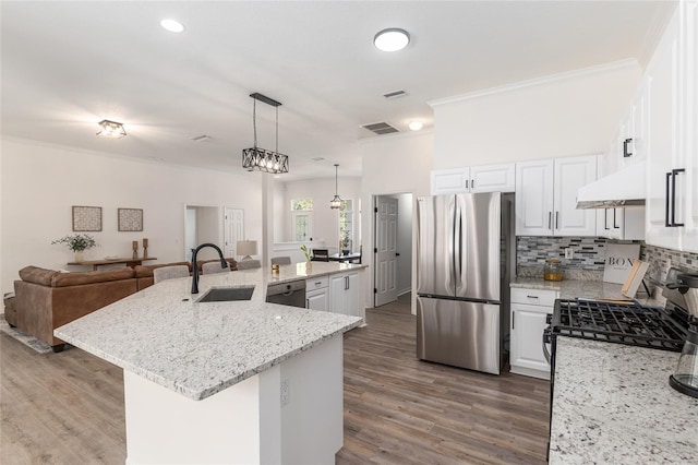 kitchen with decorative backsplash, appliances with stainless steel finishes, open floor plan, a sink, and under cabinet range hood