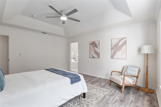 bedroom with light wood-style flooring, visible vents, baseboards, ornamental molding, and a tray ceiling