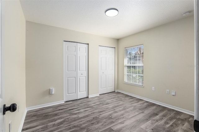 unfurnished bedroom featuring baseboards, wood finished floors, and multiple closets