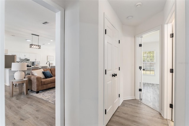 hallway featuring light wood-style flooring, recessed lighting, a sink, visible vents, and baseboards