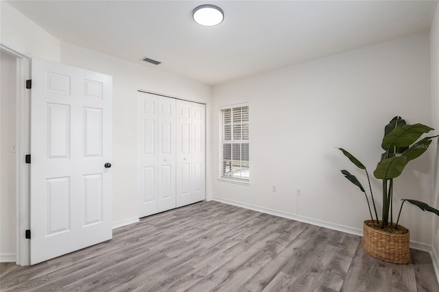 unfurnished bedroom featuring a closet, visible vents, baseboards, and wood finished floors