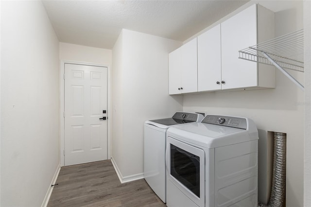 clothes washing area featuring cabinet space, washer and clothes dryer, baseboards, and wood finished floors