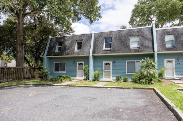 view of property with mansard roof, roof with shingles, and fence