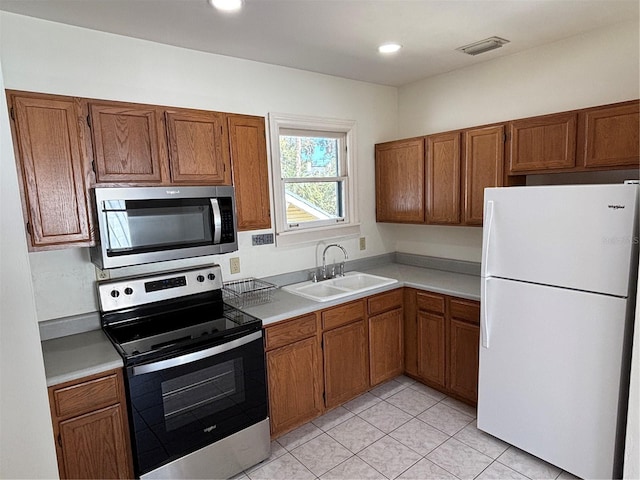 kitchen with brown cabinetry, visible vents, stainless steel appliances, and a sink