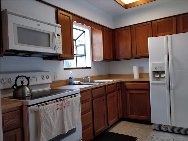 kitchen featuring brown cabinets, light countertops, light tile patterned flooring, a sink, and white appliances