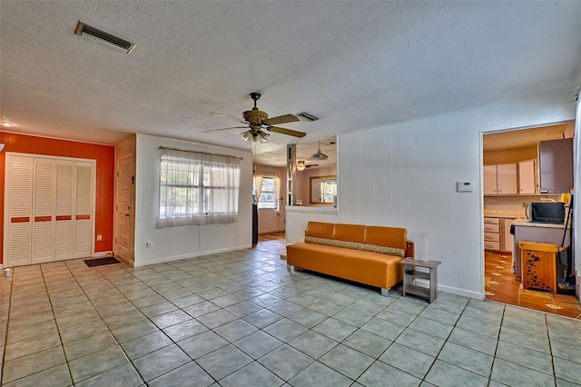 interior space with ceiling fan, a textured ceiling, light tile patterned flooring, and visible vents