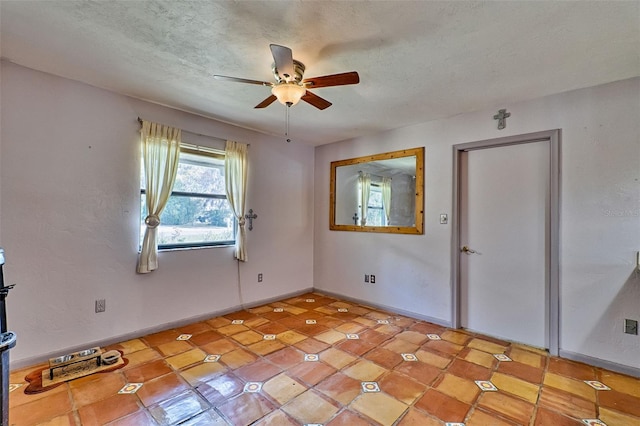 spare room featuring a textured ceiling, ceiling fan, and baseboards