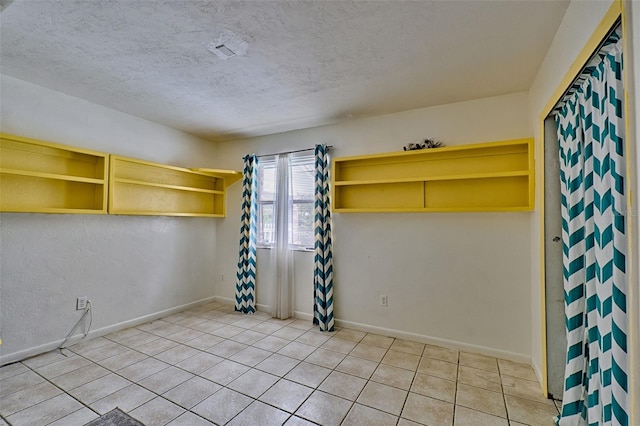 unfurnished room with a textured ceiling, light tile patterned floors, and baseboards