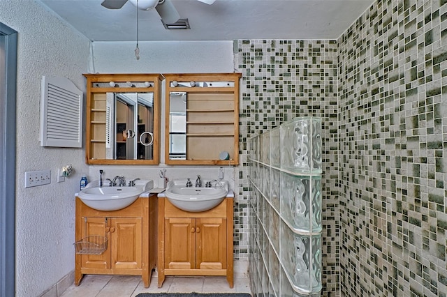 full bathroom featuring ceiling fan, a textured wall, double vanity, and a sink