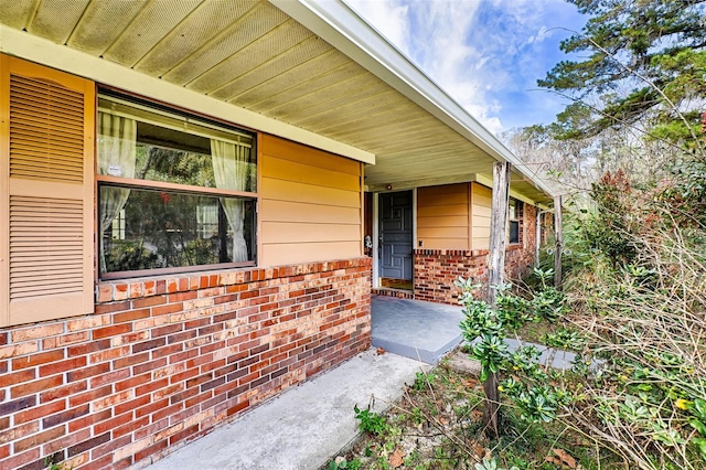 doorway to property with covered porch and brick siding