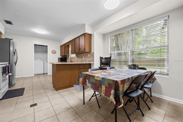 kitchen featuring washing machine and clothes dryer, visible vents, backsplash, brown cabinetry, and stainless steel fridge with ice dispenser