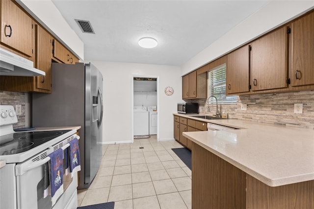 kitchen featuring visible vents, white range with electric cooktop, stainless steel microwave, washing machine and dryer, and a sink