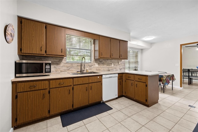 kitchen featuring light countertops, stainless steel microwave, a sink, dishwasher, and a peninsula