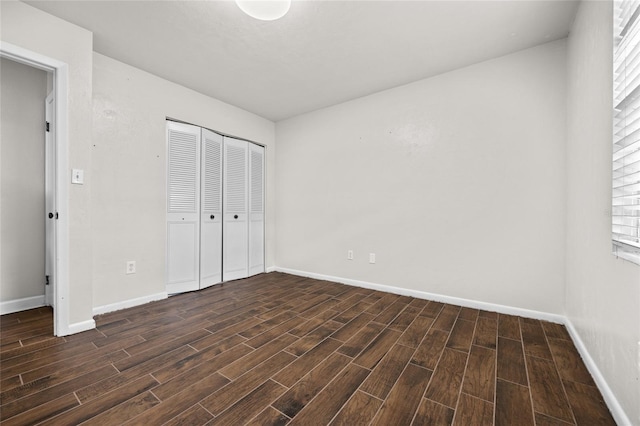 unfurnished bedroom with a closet, baseboards, and dark wood-type flooring