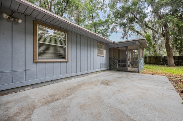 view of side of property featuring a patio, fence, and a sunroom